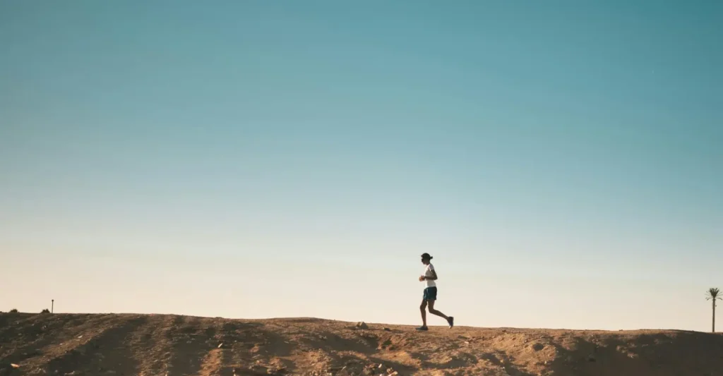 A person jogs on a sandy path with a vast blue sky above, capturing movement and freedom.