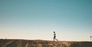 A person jogs on a sandy path with a vast blue sky above, capturing movement and freedom.