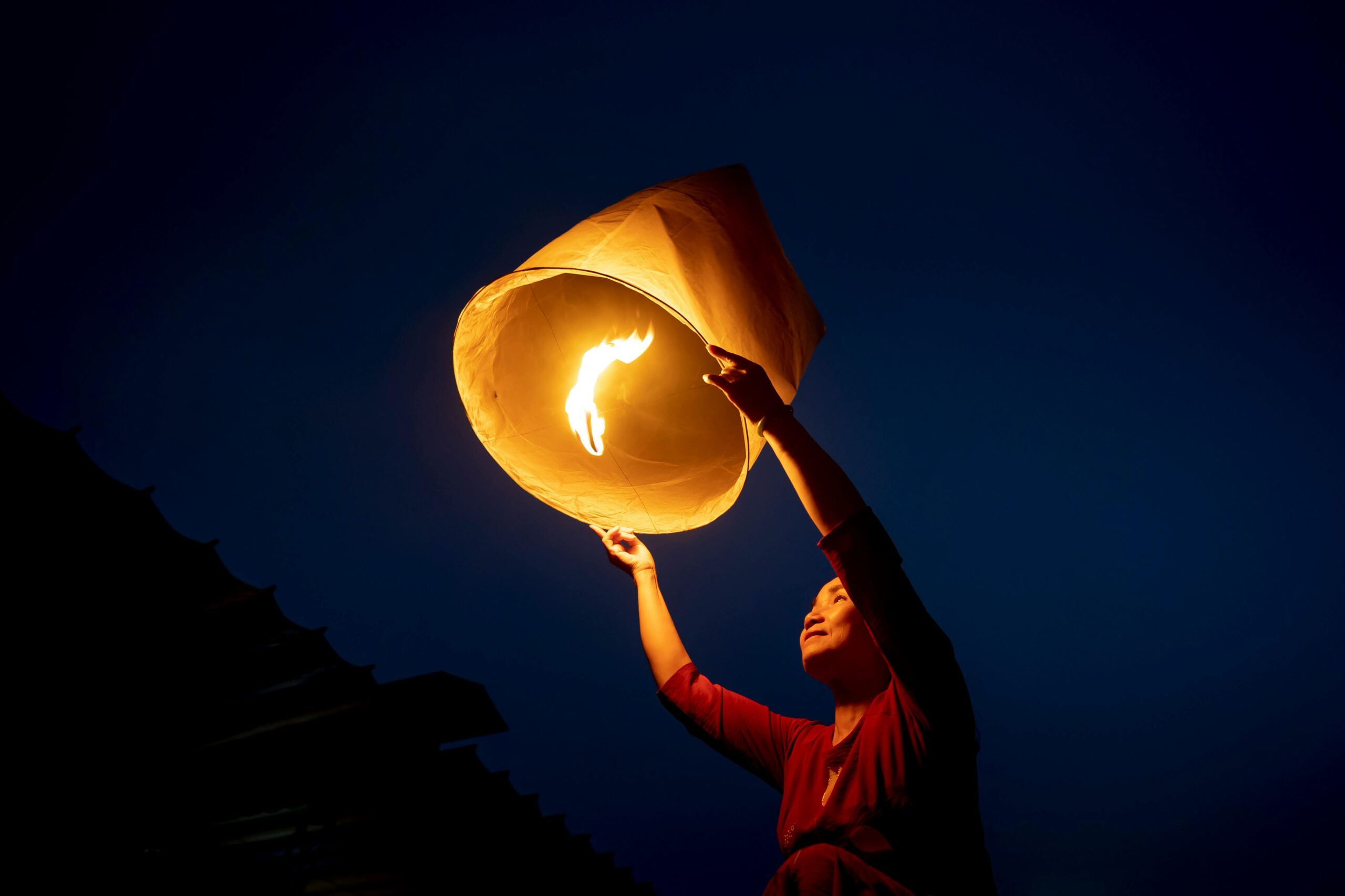A person releasing a glowing sky lantern against a dark night sky.